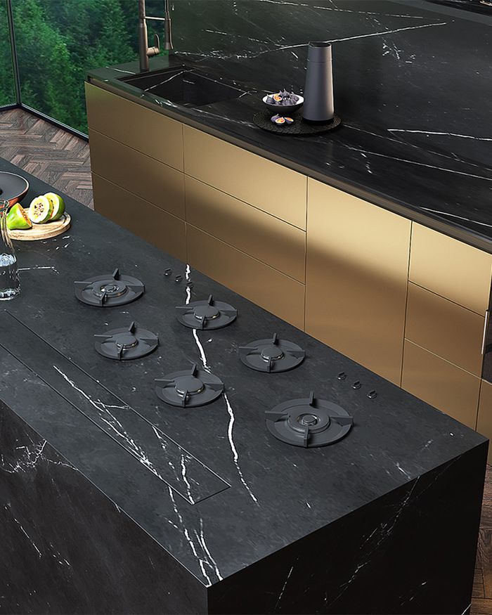 The image showcases a modern kitchen from the GOLDNESS series by Mebel Arts. The marble countertop with built-in cooking hobs highlights elegance and luxury in design. Gold detailing on the cabinets adds a sense of excellence and emits a warm glow, enhancing the aesthetic of the space. The ergonomic arrangement of the hobs and their advanced features emphasize adaptability and functionality, making it perfect for the contemporary cook.