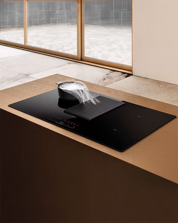 The image features a modern ceramic cooktop with an integrated absorption system, possibly from the Elica Nikolatesla series, seamlessly incorporated into an elegant kitchen surface with wooden elements. The description will focus on the sleek aesthetics and functionality of the product, as well as its adaptability to contemporary kitchen design.