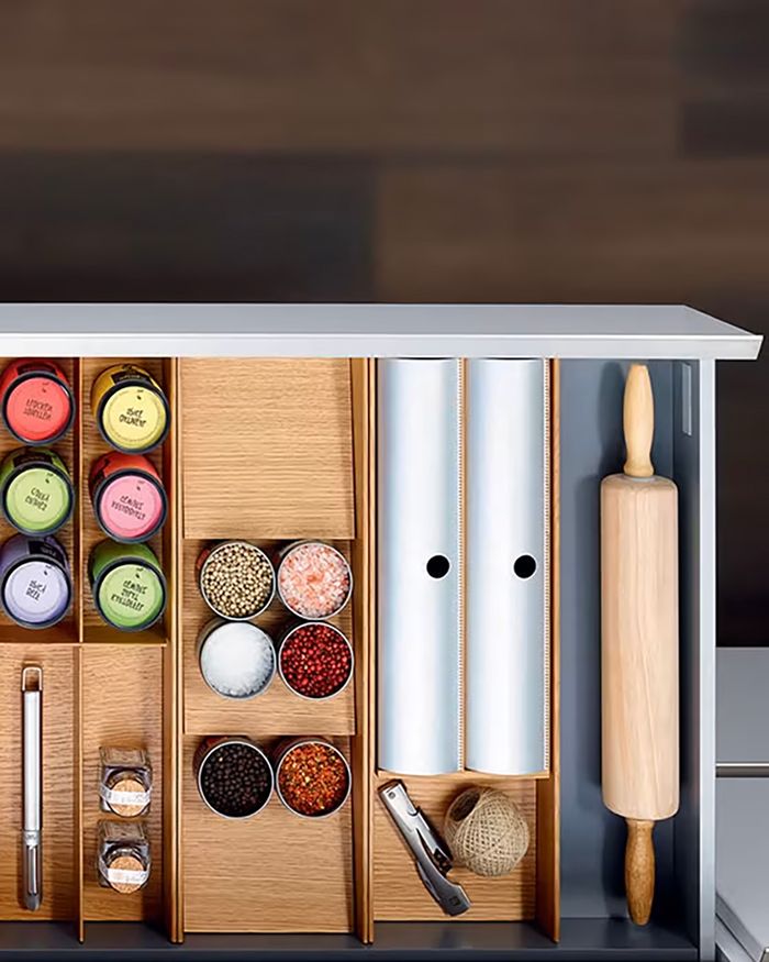 The image shows a kitchen cabinet storage system from the MosaiQ series by Kessebohmer, available through Mebel Arts. It highlights the smart organization and aesthetics of storage space with various holders for spices, foil, wrap, and other cooking items. The use of natural wood combines elegance with functionality, providing a practical and appealing solution for kitchen organization.