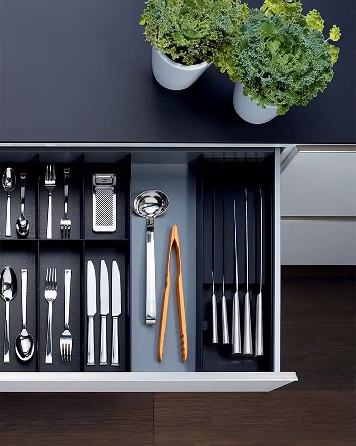 The image displays a tastefully organized knife holder with German design in a modern kitchen. The knives and cooking setups are carefully placed, offering easy access and a sleek appearance. Natural decorative details add vitality and freshness to the space.
