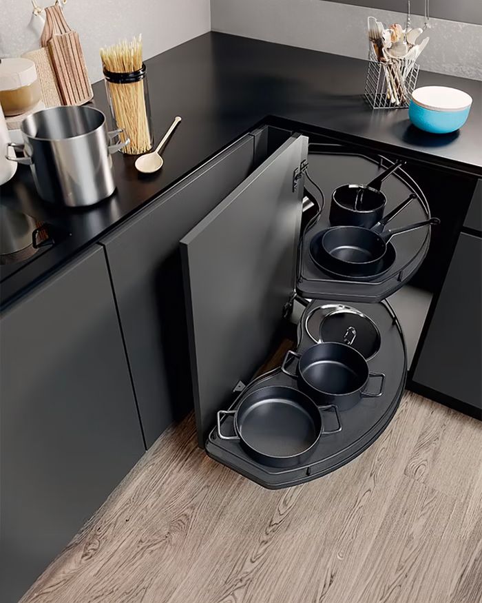 Cette image présente un mécanisme de rangement d'angle innovant de la série Cornerstone de Vauth Sagel, intégré dans un cadre de cuisine élégant. Le système de rangement est ouvert, dévoilant trois casseroles métalliques noires. Mebel Arts utilise ce mécanisme pour offrir adaptabilité, esthétique élégante et fonctionnalité accrue dans le mobilier de cuisine qu'elle conçoit. Cette solution aide à économiser de l'espace et à maintenir un environnement ordonné et organisé.