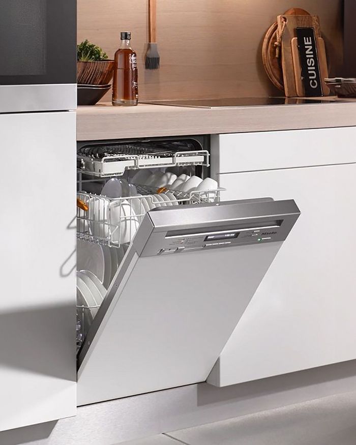 The built-in dishwasher from Mebel Arts perfectly complements the minimalist aesthetic of your modern kitchen. The image depicts the interior of the dishwasher filled with clean dishes, highlighting its high performance and clever layout. The white dishwasher is seamlessly integrated into a white kitchen surface, providing a clean and consistent appearance. The contemporary design and simple lines add an understated style, while the technology and performance delivered meet the expectations of the most demanding users.