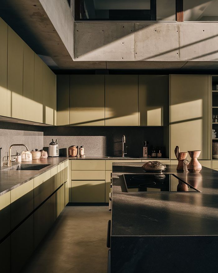 A kitchen with an island, black countertops, and light-colored cabinets. The combination of materials and lighting creates a modern and warm atmosphere. By Mebel Arts.