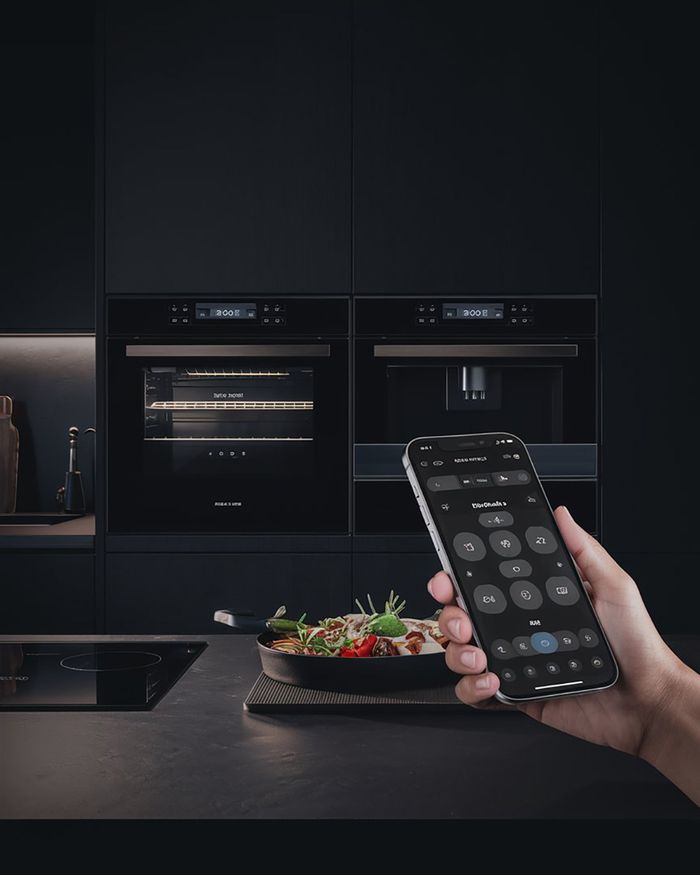 Fours à micro-ondes avec commande intelligente via téléphone portable, dans une cuisine noire avec un plat préparé devant.