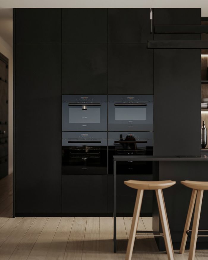 Built-in black ovens in a modern kitchen with wooden stools and glossy surface finishes.